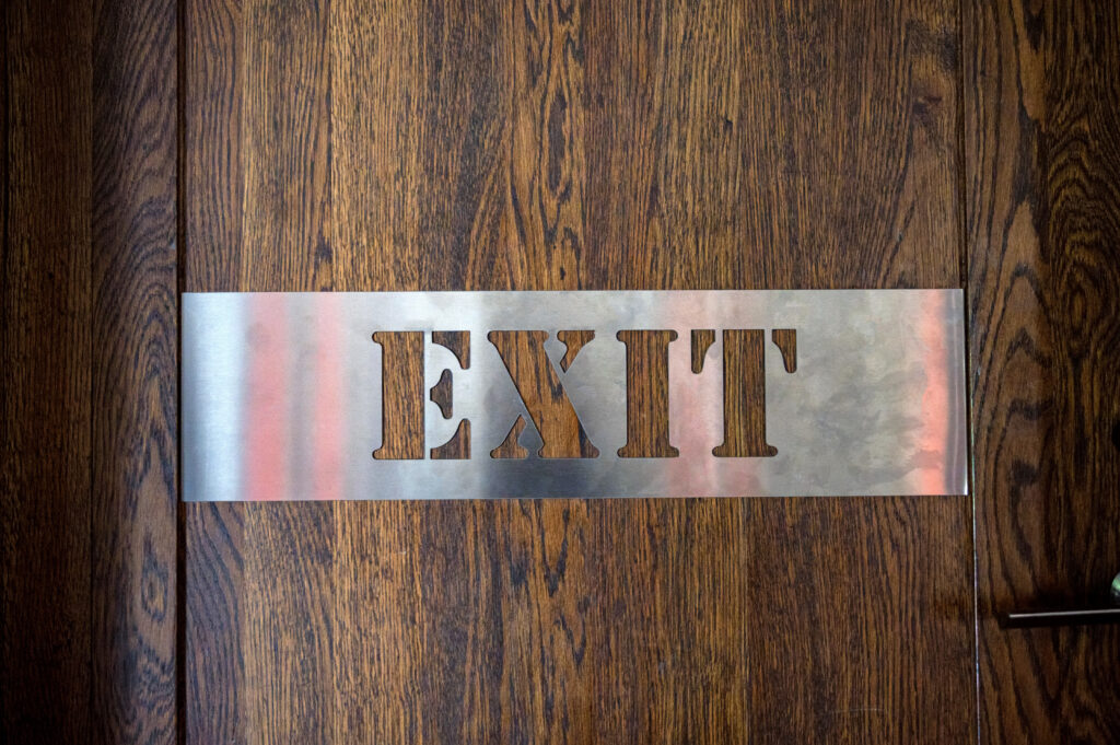 Metal EXIT sign mounted on a wooden door representing employee turnover in small businesses